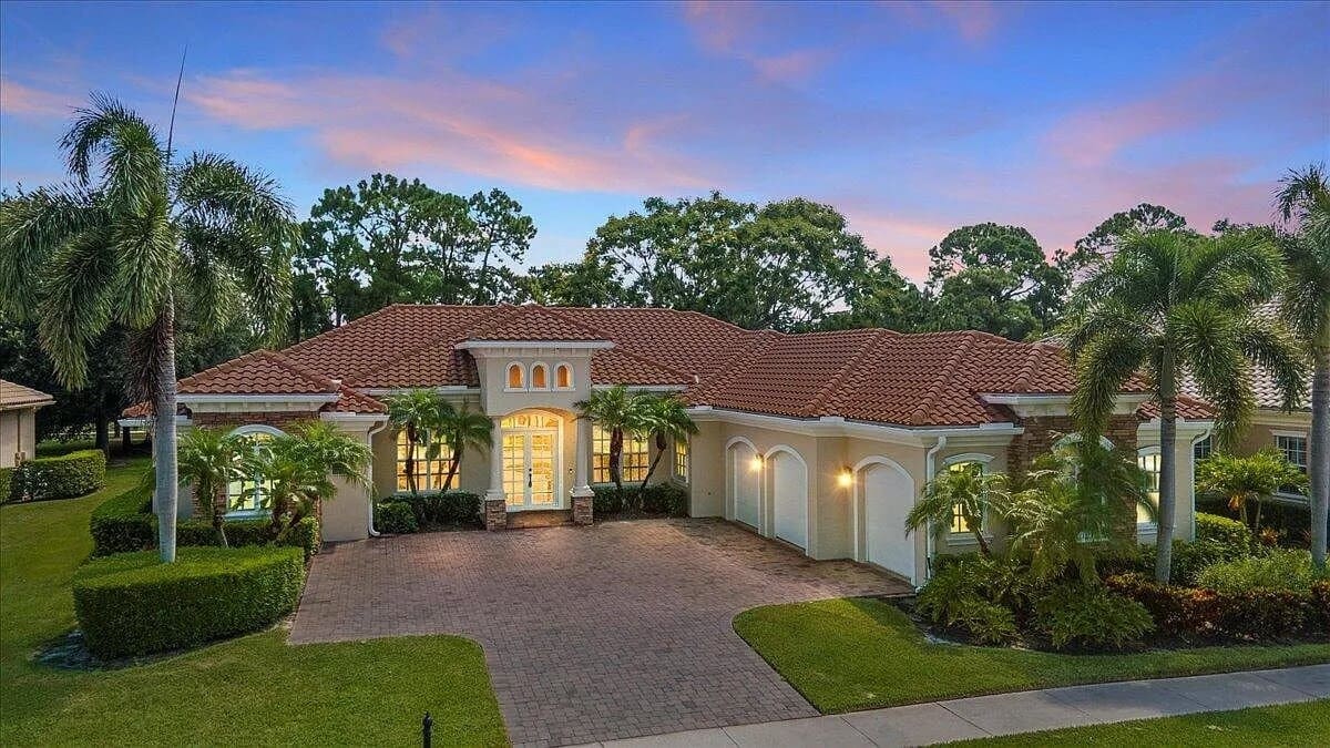 Single-story house with red-tiled roof, palm trees, and a paved driveway at sunset.