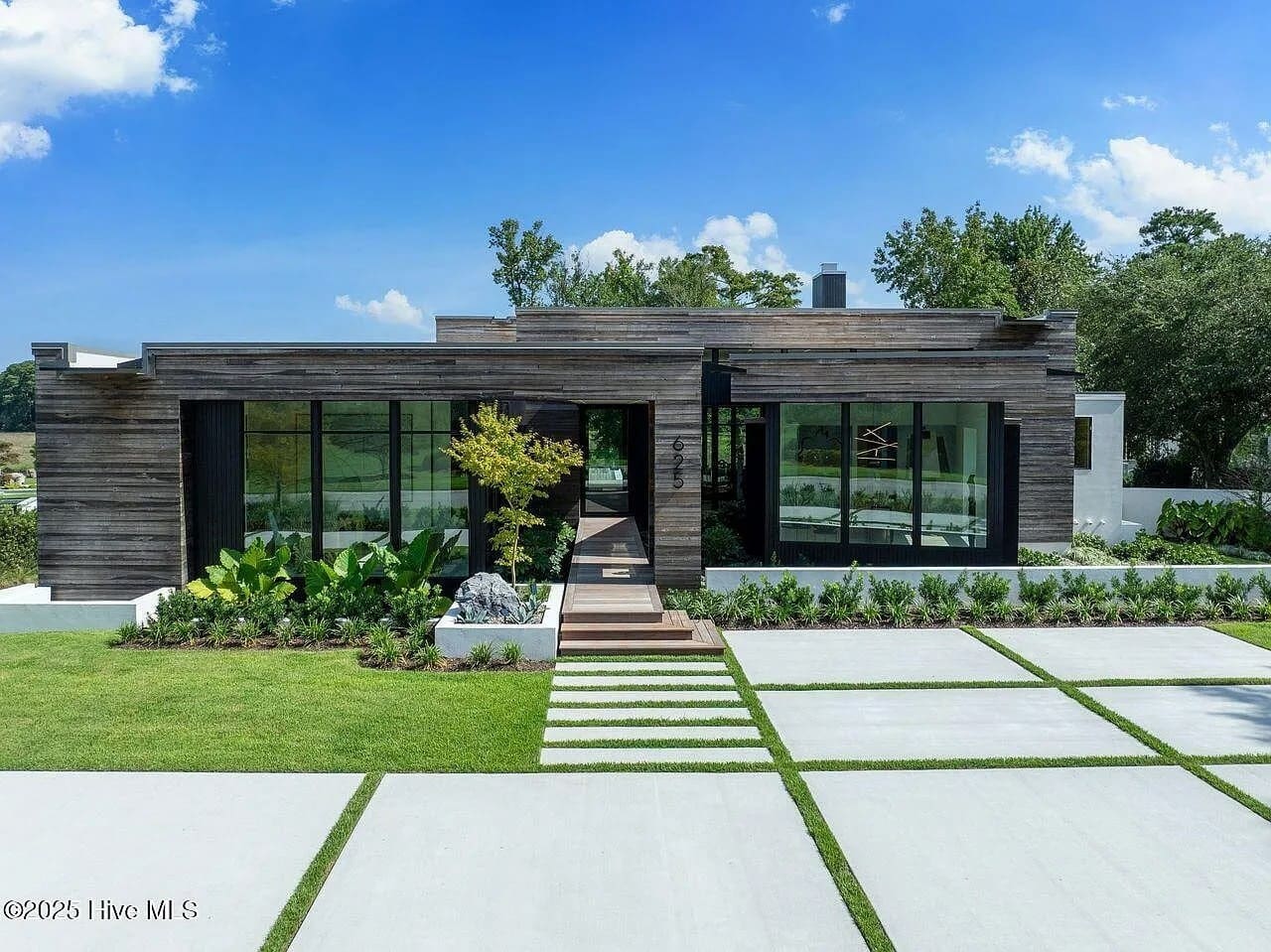 Modern house with large windows, wooden accents, and a landscaped front yard with stepping stones.