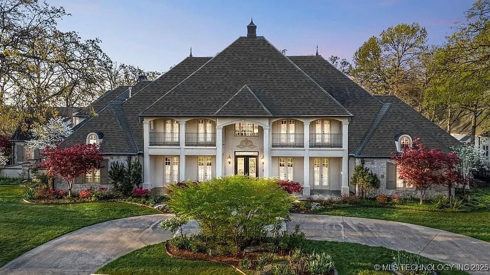 Large, elegant two-story house with a steep roof, surrounded by landscaped gardens and a circular driveway.
