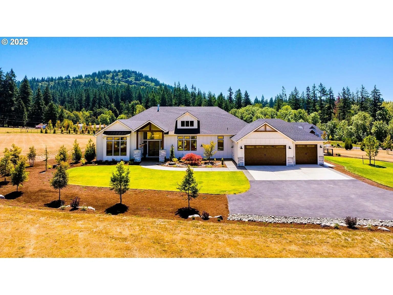 A large, modern house with a manicured lawn, surrounded by trees and hills.