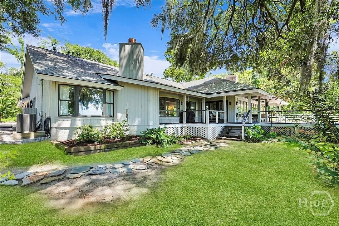 A charming house with a wraparound porch, surrounded by lush greenery and trees.