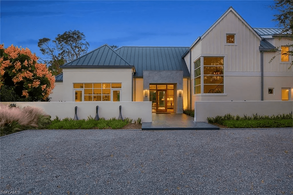 Modern house with large windows, metal roof, and landscaped front yard at dusk.
