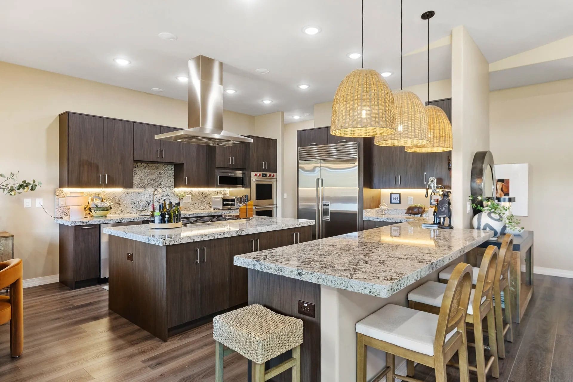 Modern kitchen with dark wood cabinets, granite countertops, stainless steel appliances, and wicker pendant lights.