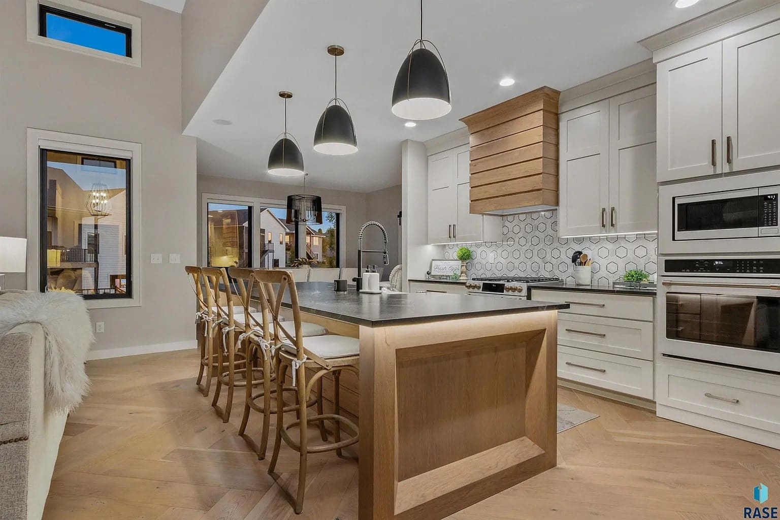 Modern kitchen with island seating, pendant lights, and stainless steel appliances. Light wood and white cabinetry.