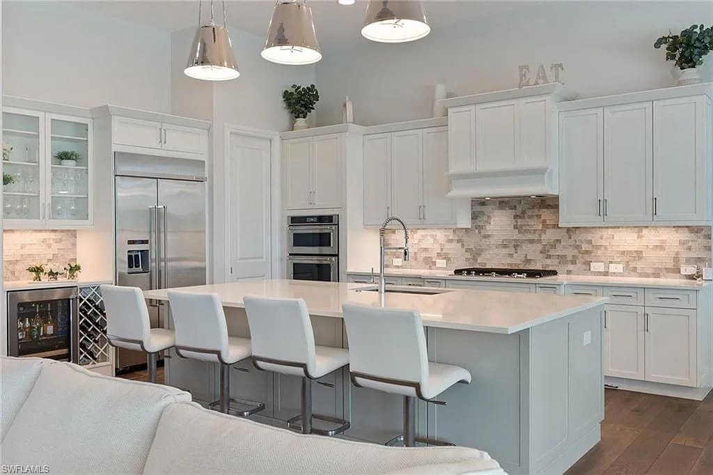 Modern kitchen with white cabinets, island with bar stools, stainless steel appliances, and pendant lighting.

