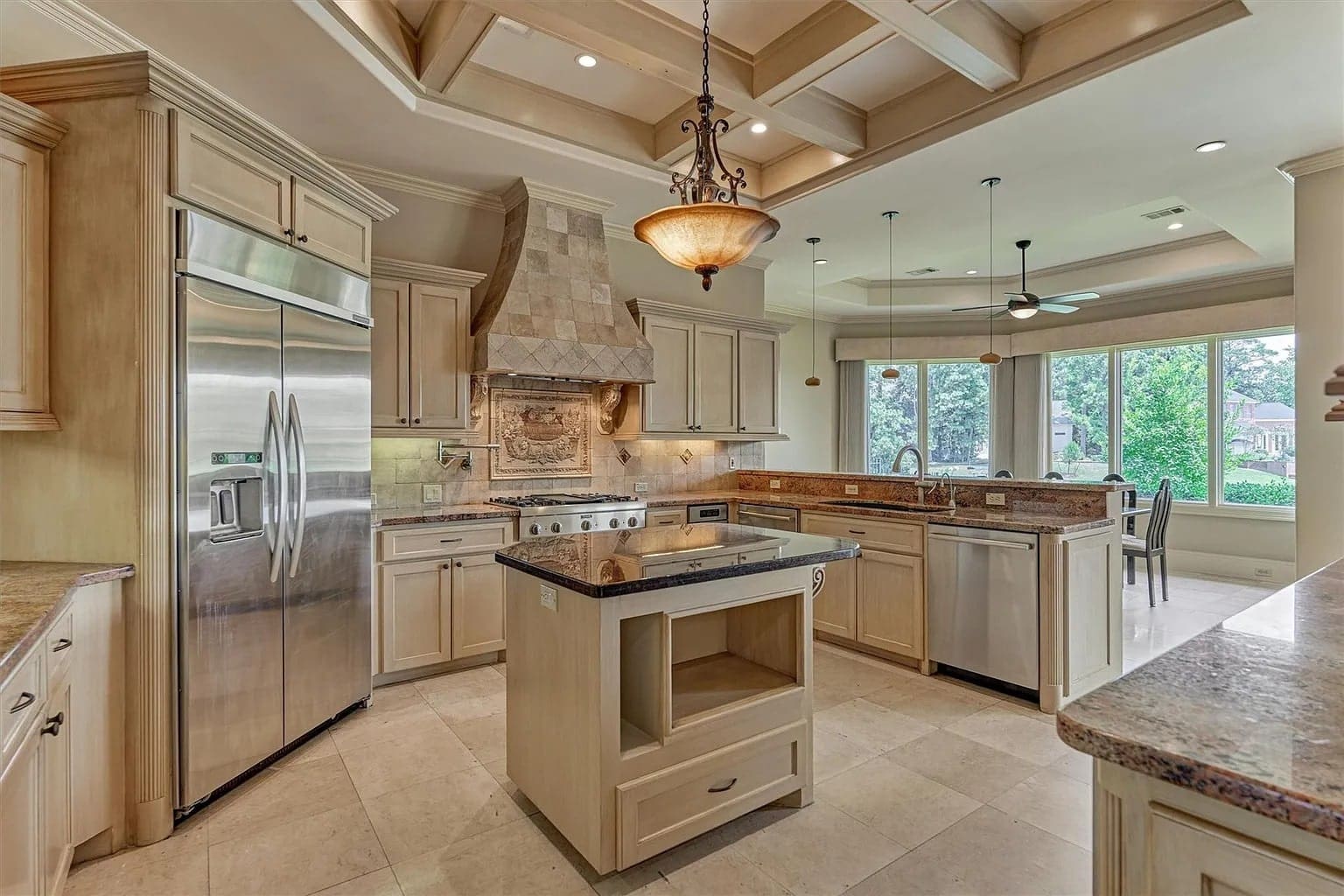 Spacious modern kitchen with island, stainless steel appliances, and large windows overlooking greenery.
