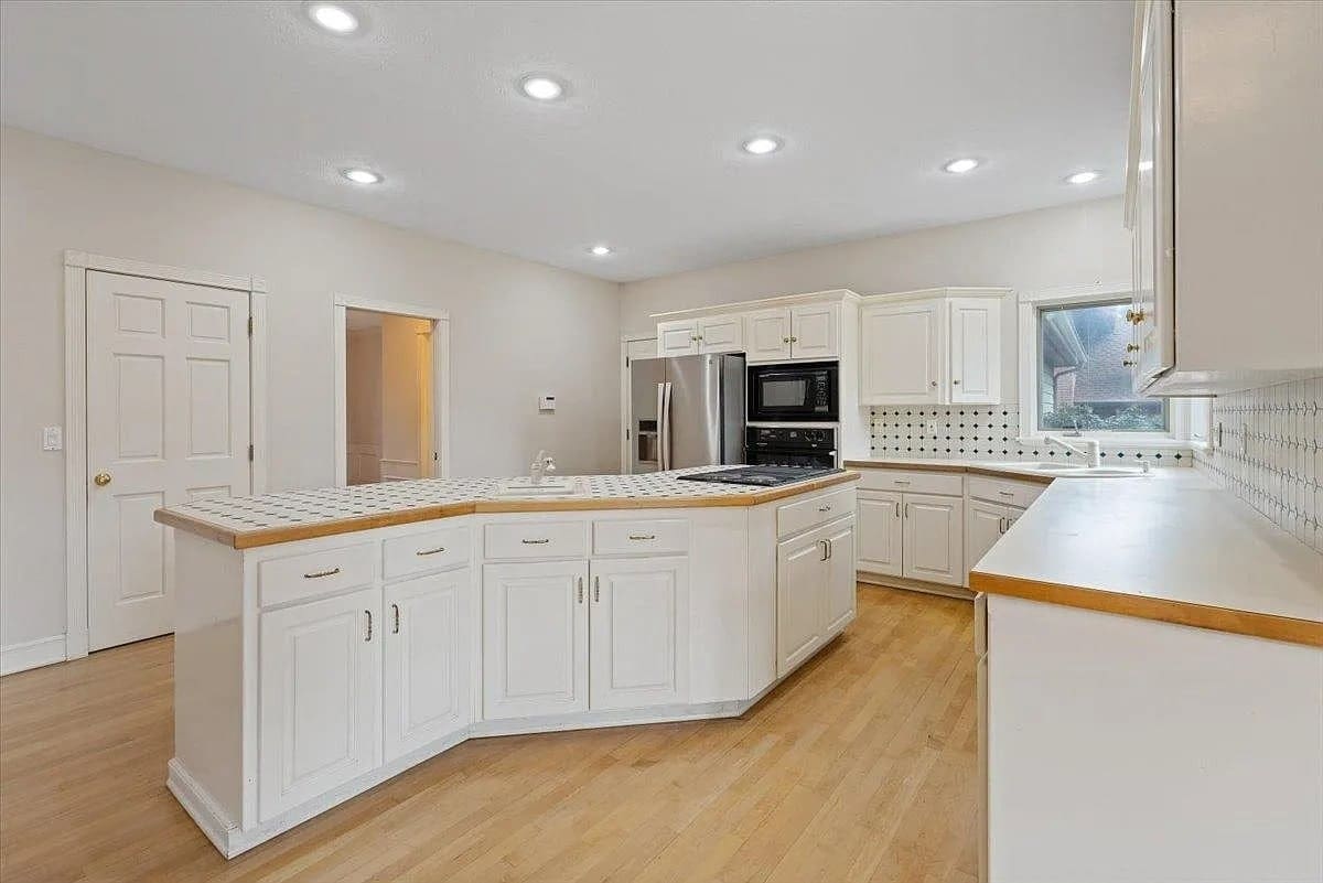 Spacious kitchen with white cabinets, wooden countertops, and a central island on a wooden floor.
