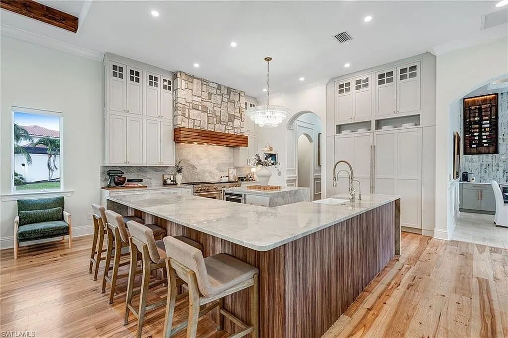 Spacious modern kitchen with large island, wooden floors, stone backsplash, and chandelier lighting.