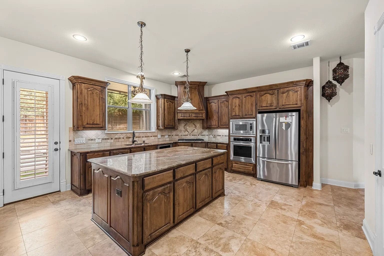 Spacious kitchen with wooden cabinets, marble island, stainless steel appliances, and tile flooring.

