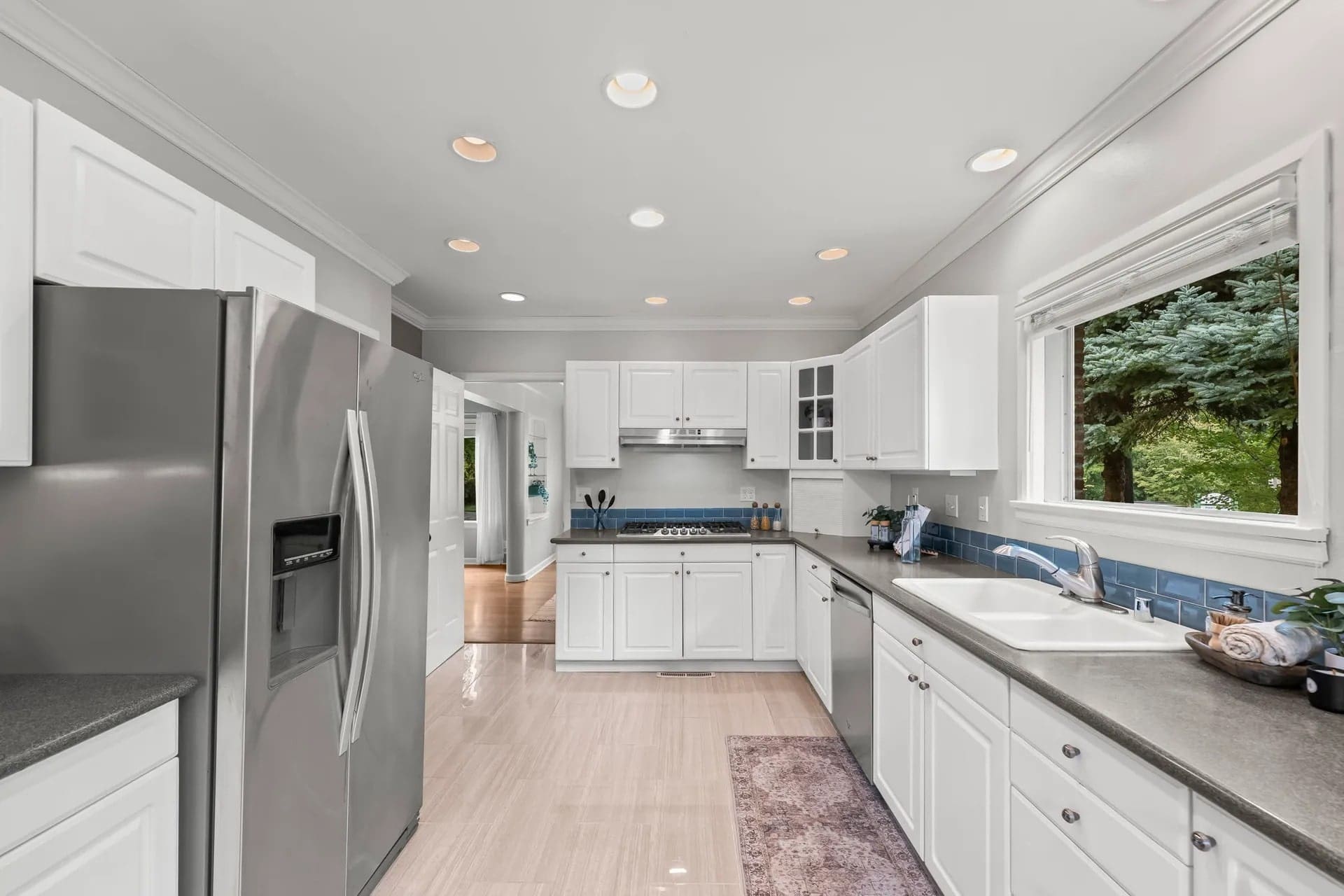 Modern kitchen with white cabinets, stainless steel appliances, and large window overlooking greenery.
