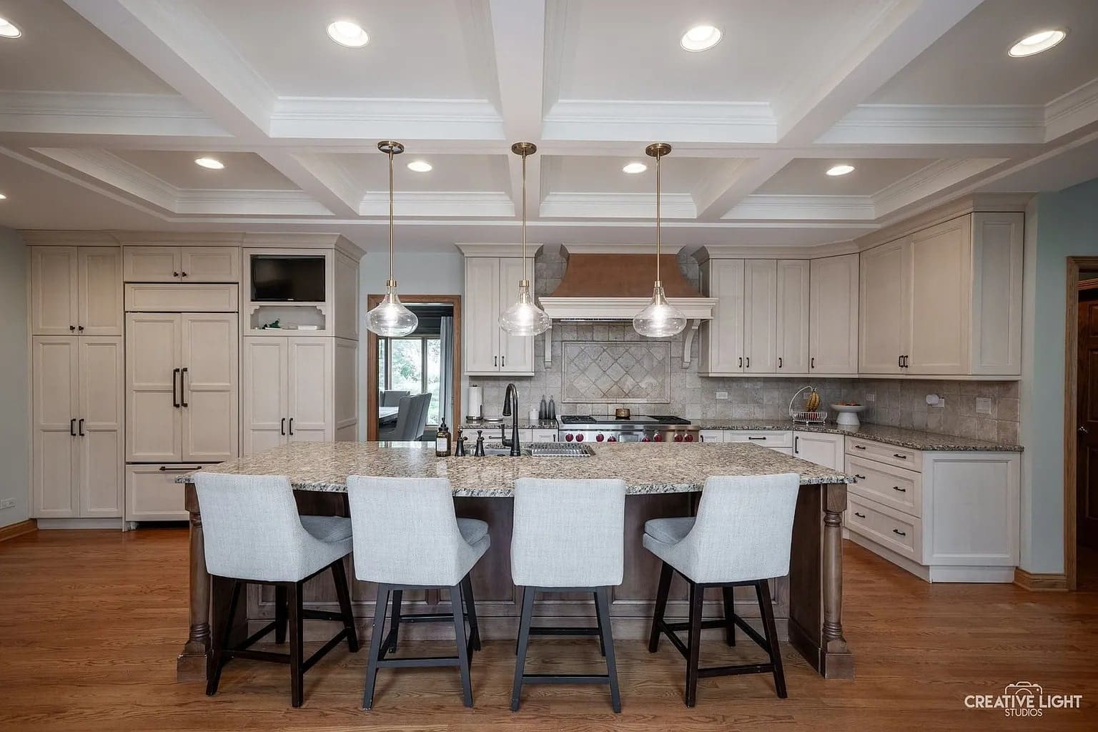 Modern kitchen with a large island, barstools, pendant lights, and white cabinetry.
