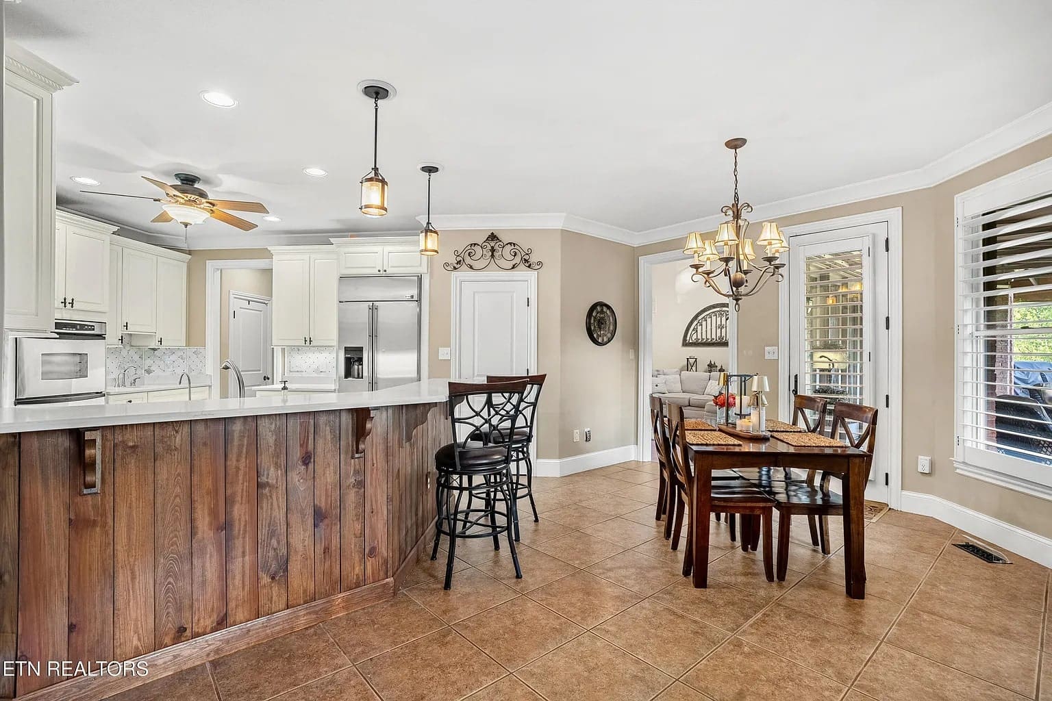 Kitchen and dining area with wooden accents, bar stools, dining table, and chandelier lighting.