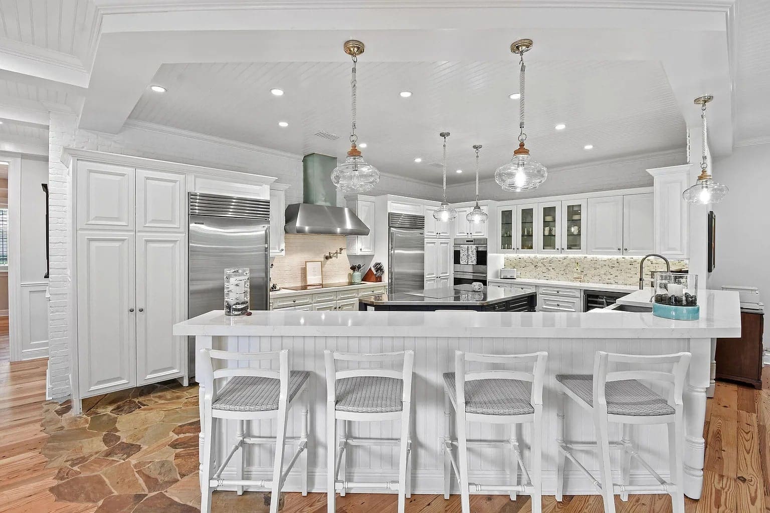 Spacious white kitchen with a large island, bar stools, and modern appliances.
