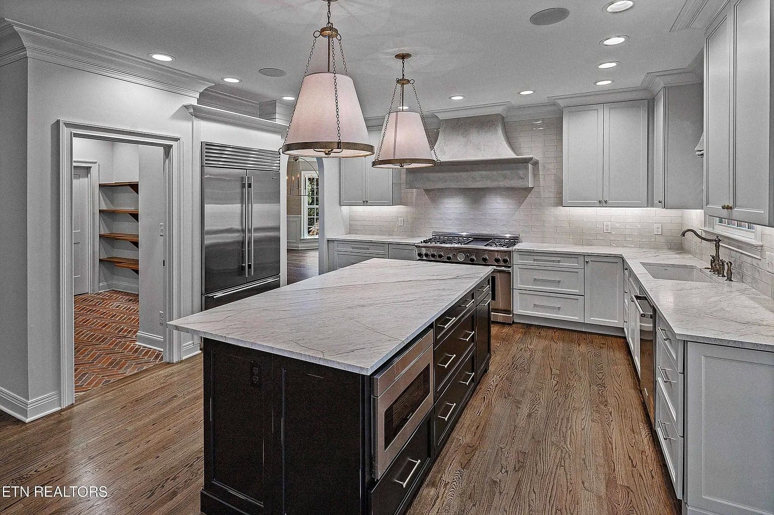 Modern kitchen with marble island, stainless steel appliances, white cabinetry, and wooden floors.