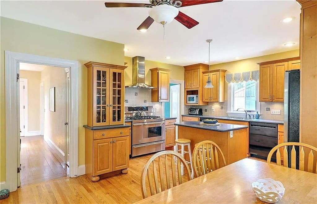 Spacious kitchen with wooden cabinets, stainless steel appliances, dining table, and ceiling fan.
