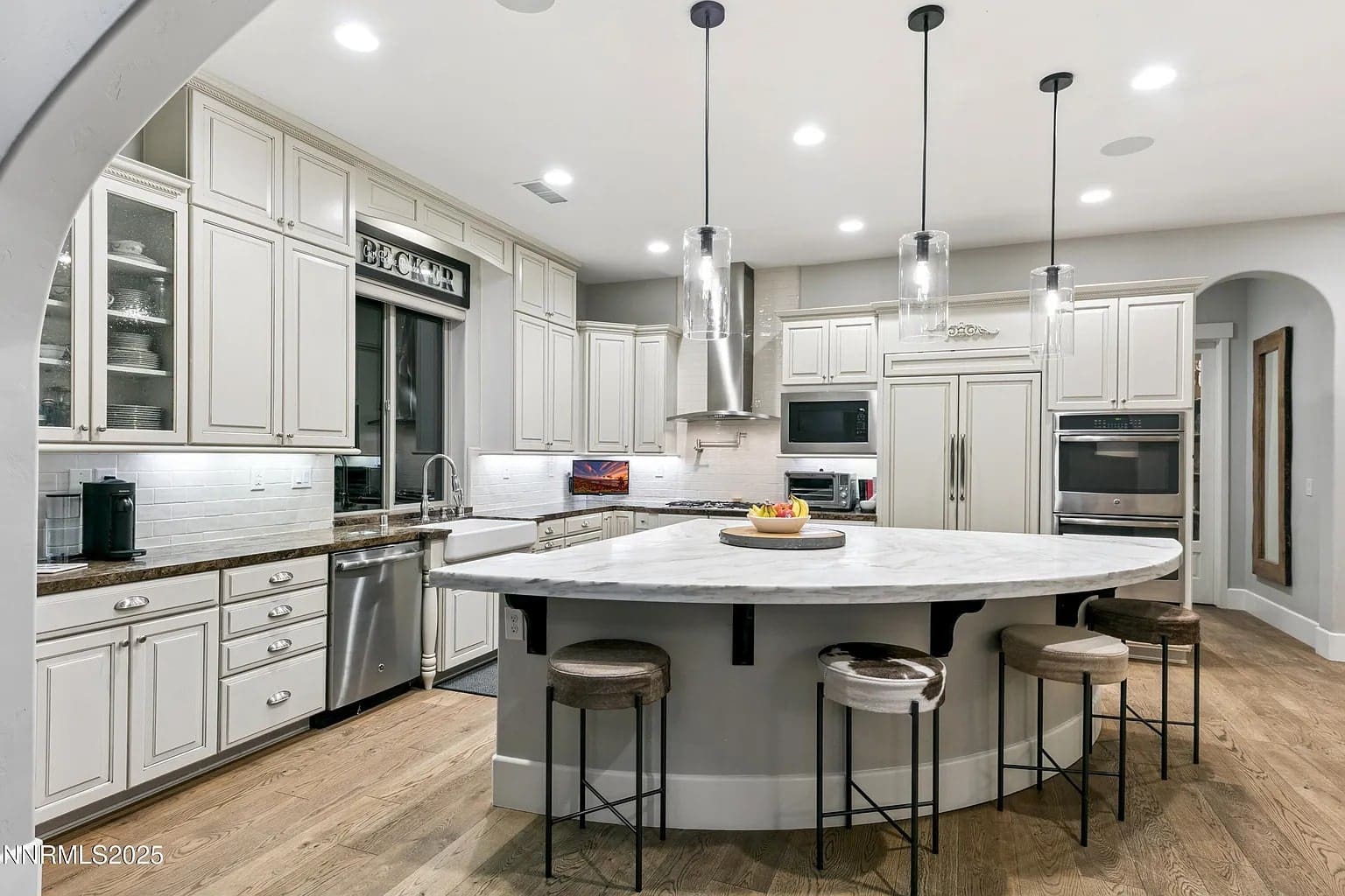 Modern kitchen with white cabinets, large curved island, bar stools, and stainless steel appliances.