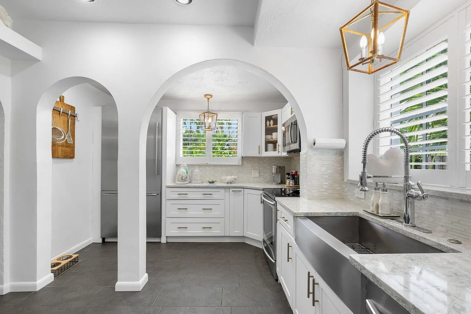 Modern white kitchen with stainless steel appliances, farmhouse sink, and arched doorways.
