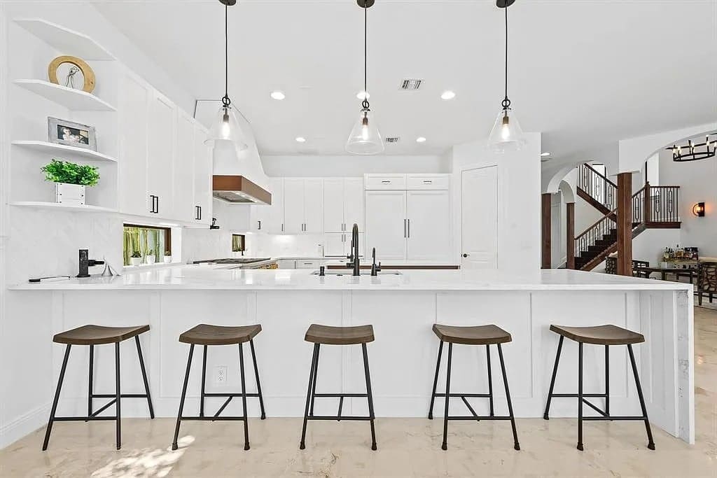 Modern kitchen with white cabinets, large island, pendant lights, and five bar stools.
