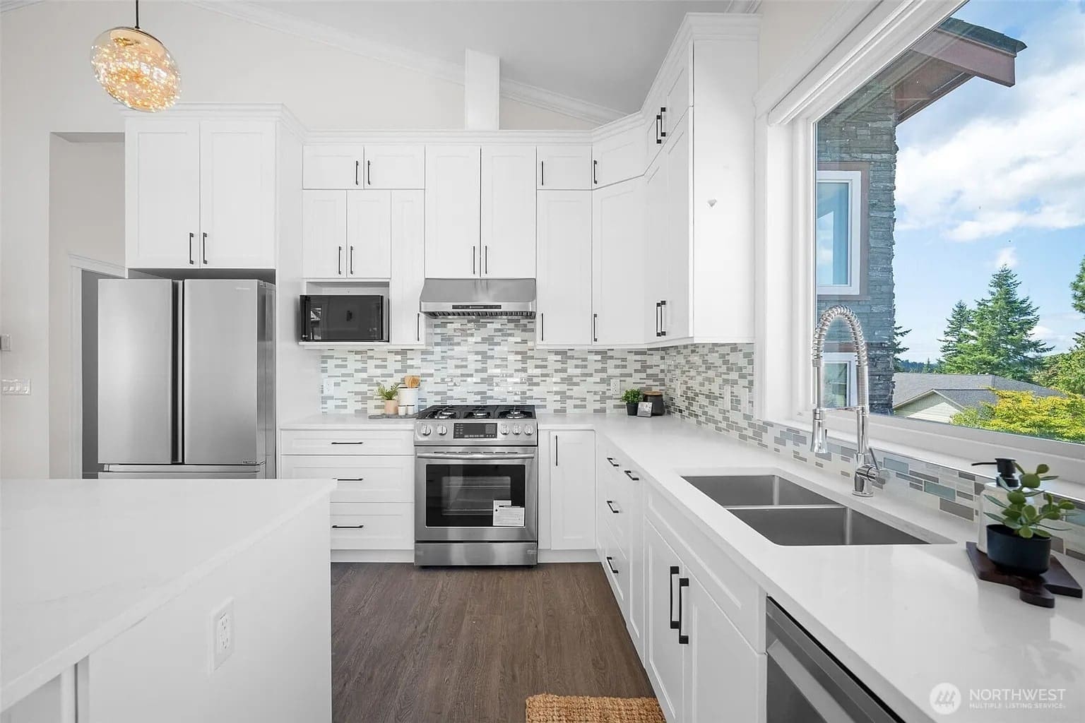 Modern kitchen with white cabinets, stainless steel appliances, large window, and a mosaic tile backsplash.
