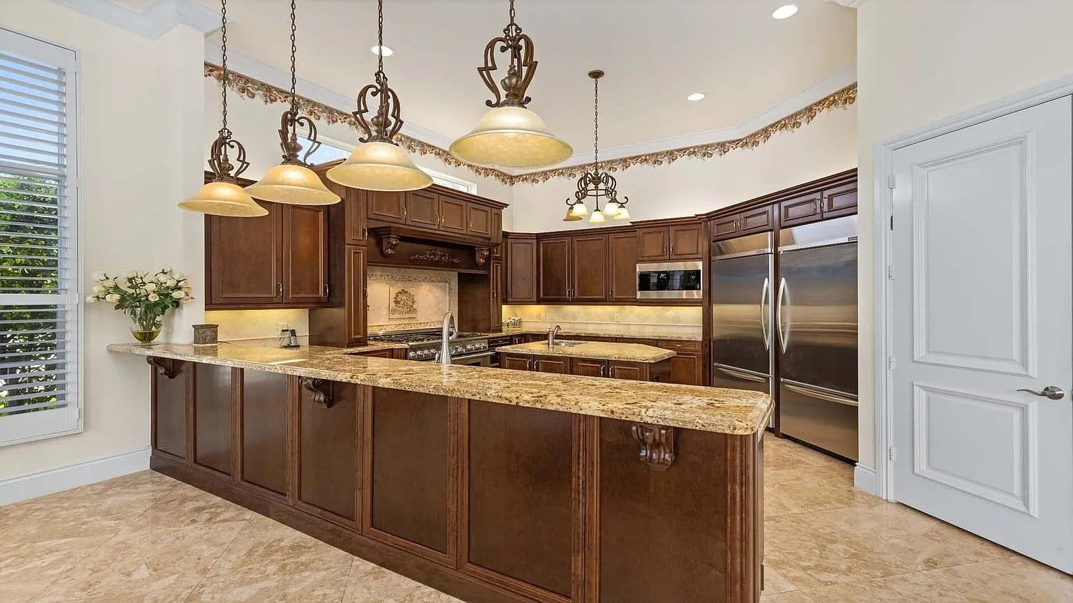 Spacious kitchen with wooden cabinets, granite countertops, stainless steel appliances, and hanging pendant lights.
