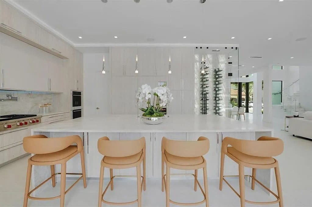 Modern kitchen with light wood cabinetry, island with tan chairs, and a wall-mounted wine rack.
