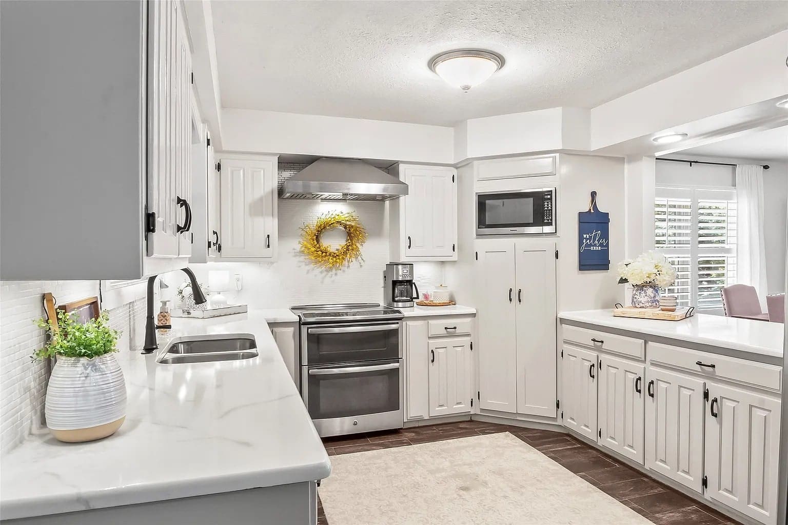 Modern kitchen with white cabinets, stainless steel appliances, and decorative wreath above stove.
