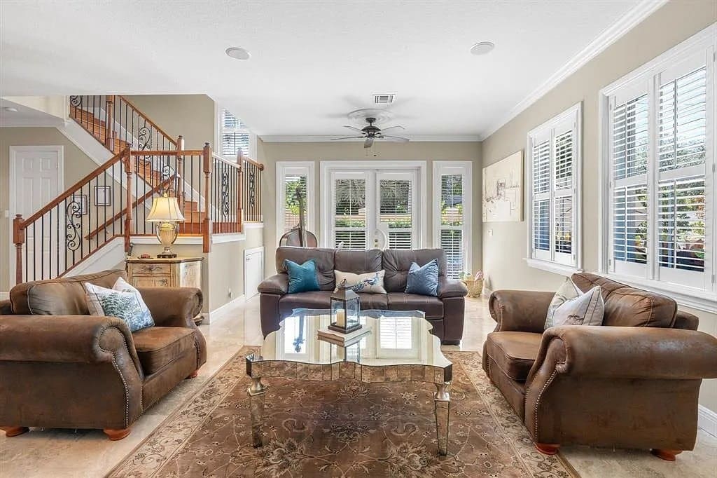 Spacious living room with brown leather furniture, glass coffee table, and large windows.
