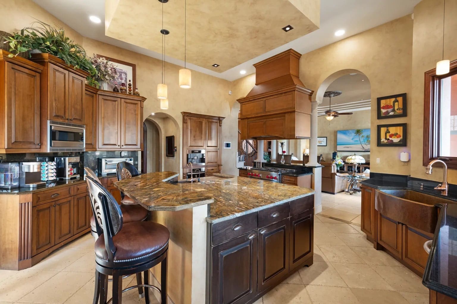 Spacious kitchen with wooden cabinets, marble countertops, bar stools, and modern appliances.
