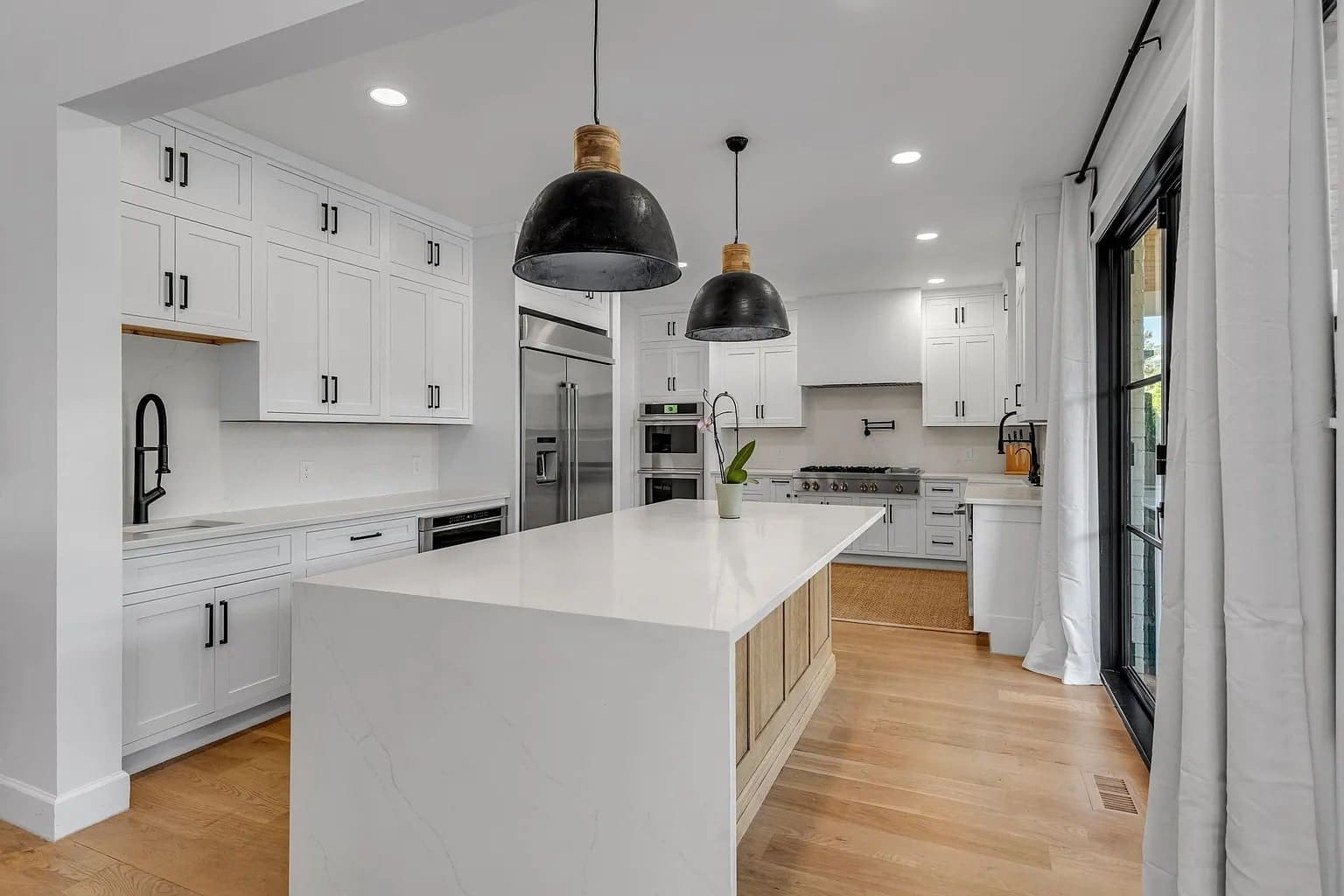 Modern kitchen with white cabinets, large island, black pendant lights, and stainless steel appliances.
