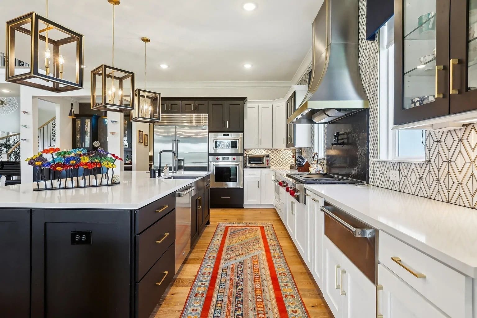 Modern kitchen with a large island, pendant lights, and a colorful rug on wooden floor.
