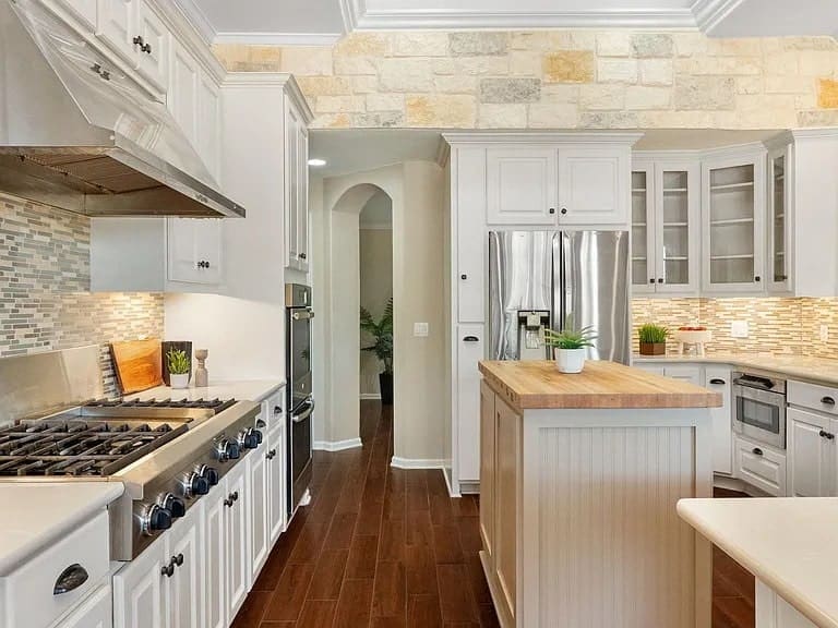 Modern kitchen with stainless steel appliances, wooden floors, and a central island with a plant.
