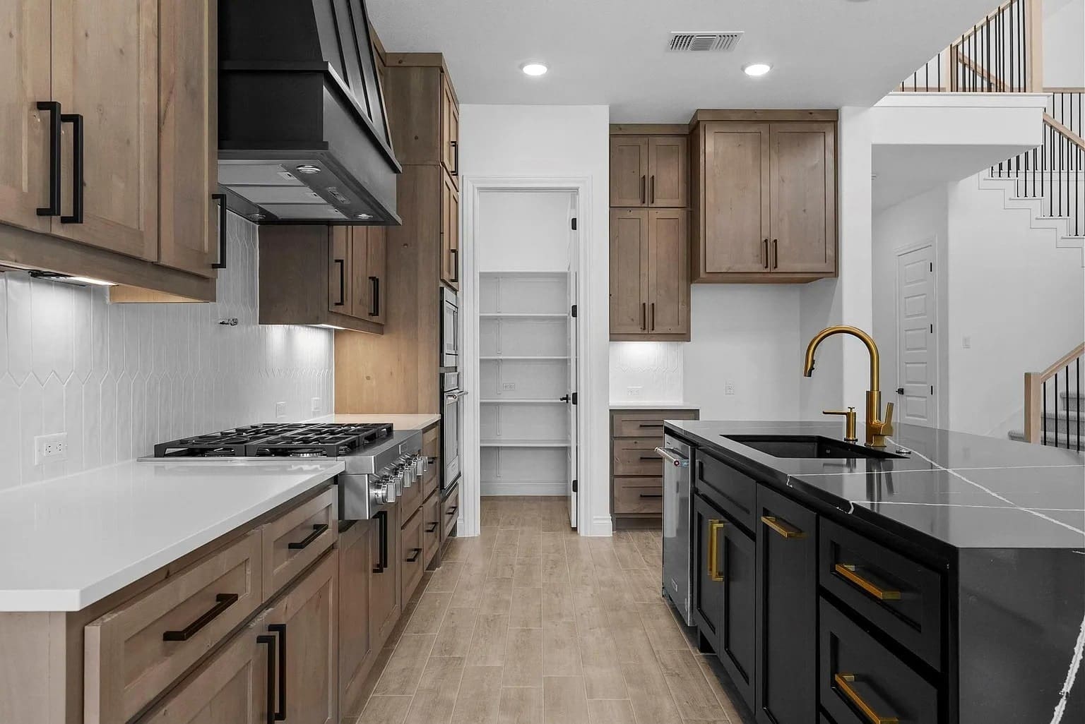 Modern kitchen with wooden cabinets, black island, gold faucet, and a walk-in pantry.
