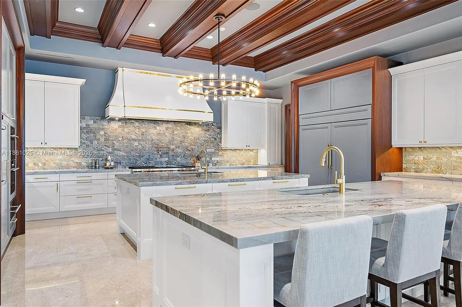 Modern kitchen with marble countertops, white cabinets, stone backsplash, and a circular chandelier.
