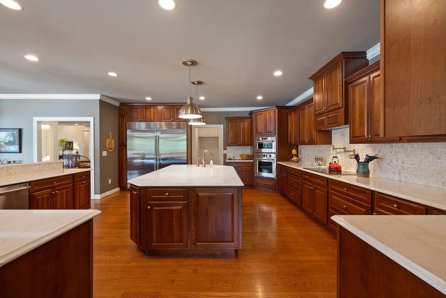 Spacious kitchen with wooden cabinets, large island, stainless steel appliances, and hardwood floors.
