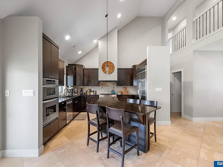 Modern kitchen with dark wood cabinets, island with chairs, stainless steel appliances, and vaulted ceiling.
