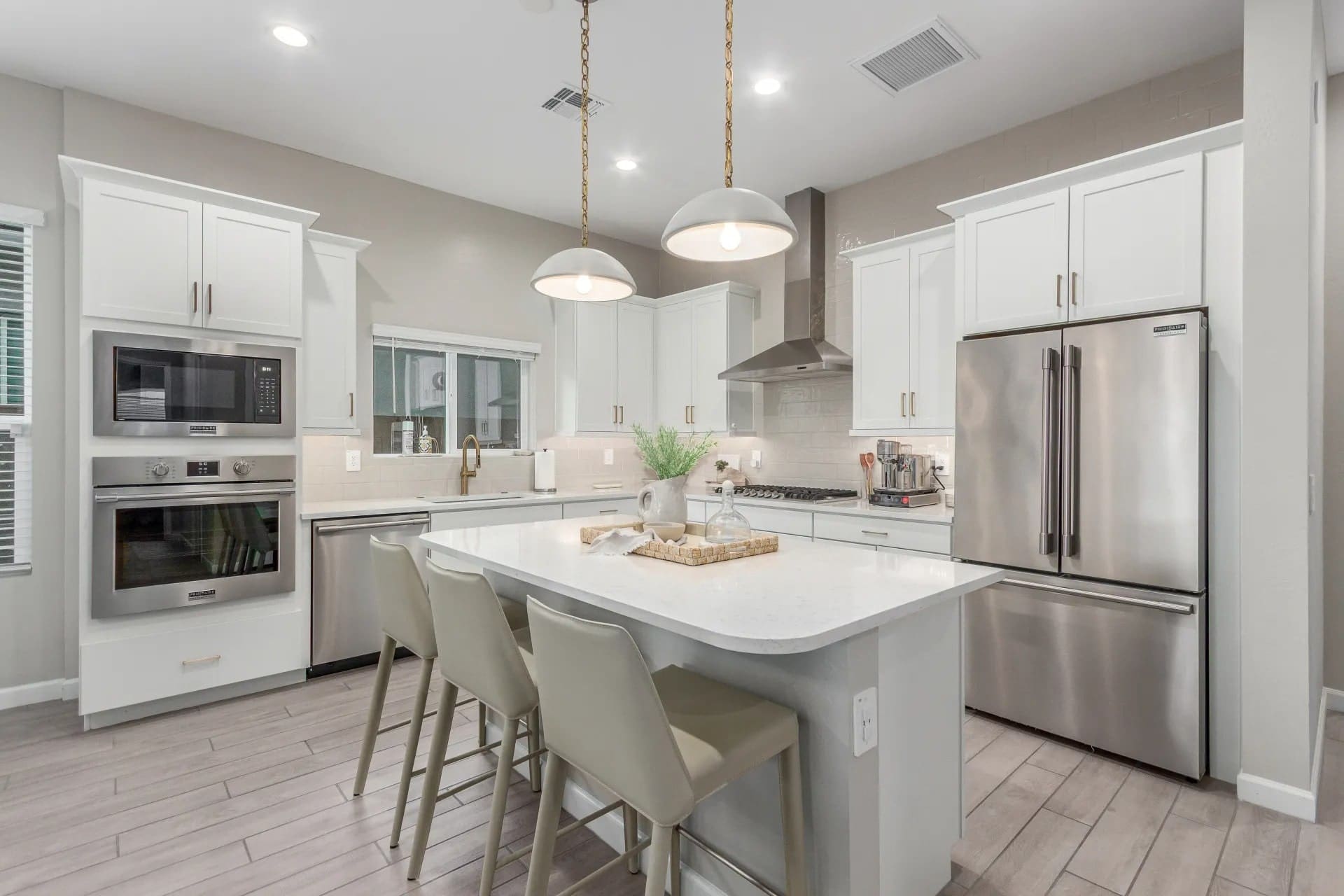Modern kitchen with white cabinets, stainless steel appliances, and a central island with three chairs.