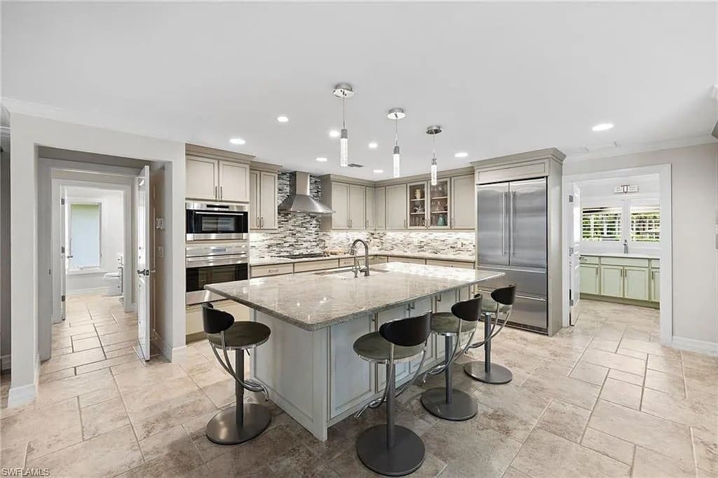 Modern kitchen with large island, bar stools, stainless steel appliances, and tiled floor.
