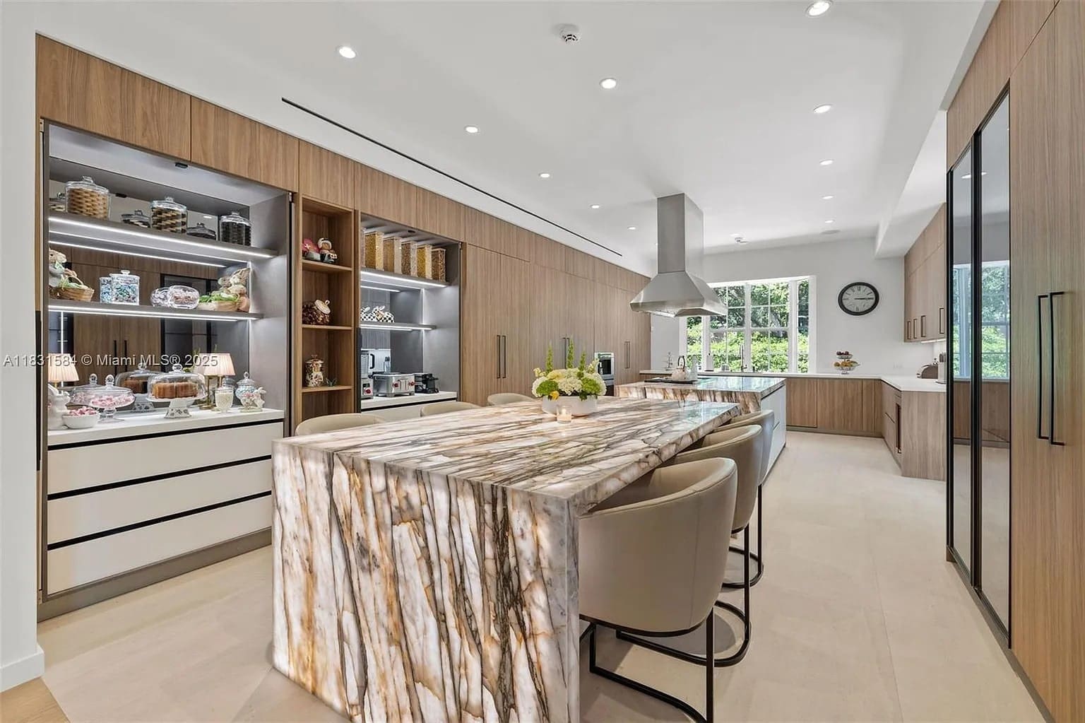 Modern kitchen with a large marble island, wooden cabinets, and open shelves displaying decor items.