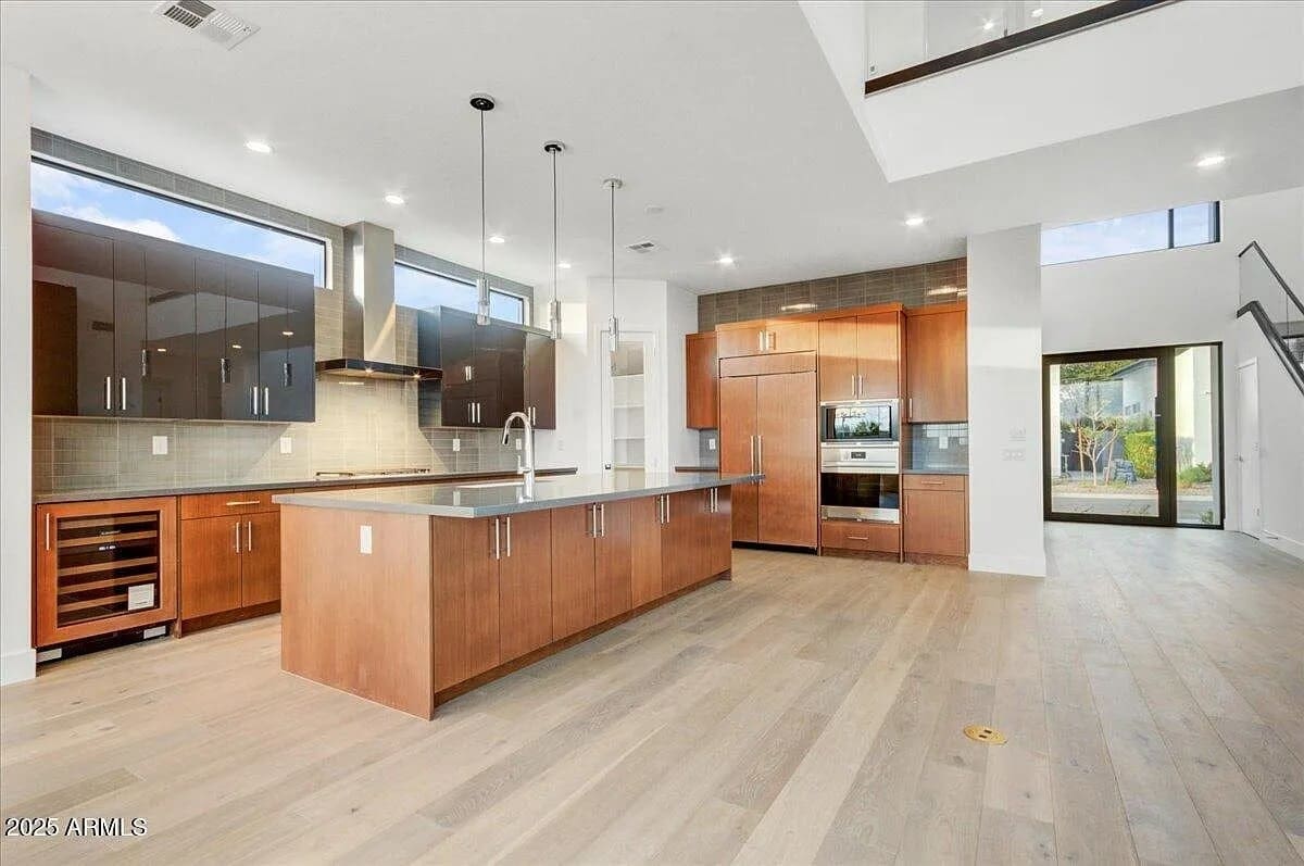 Modern kitchen with wooden cabinets, island, stainless steel appliances, and large windows. Open floor plan.
