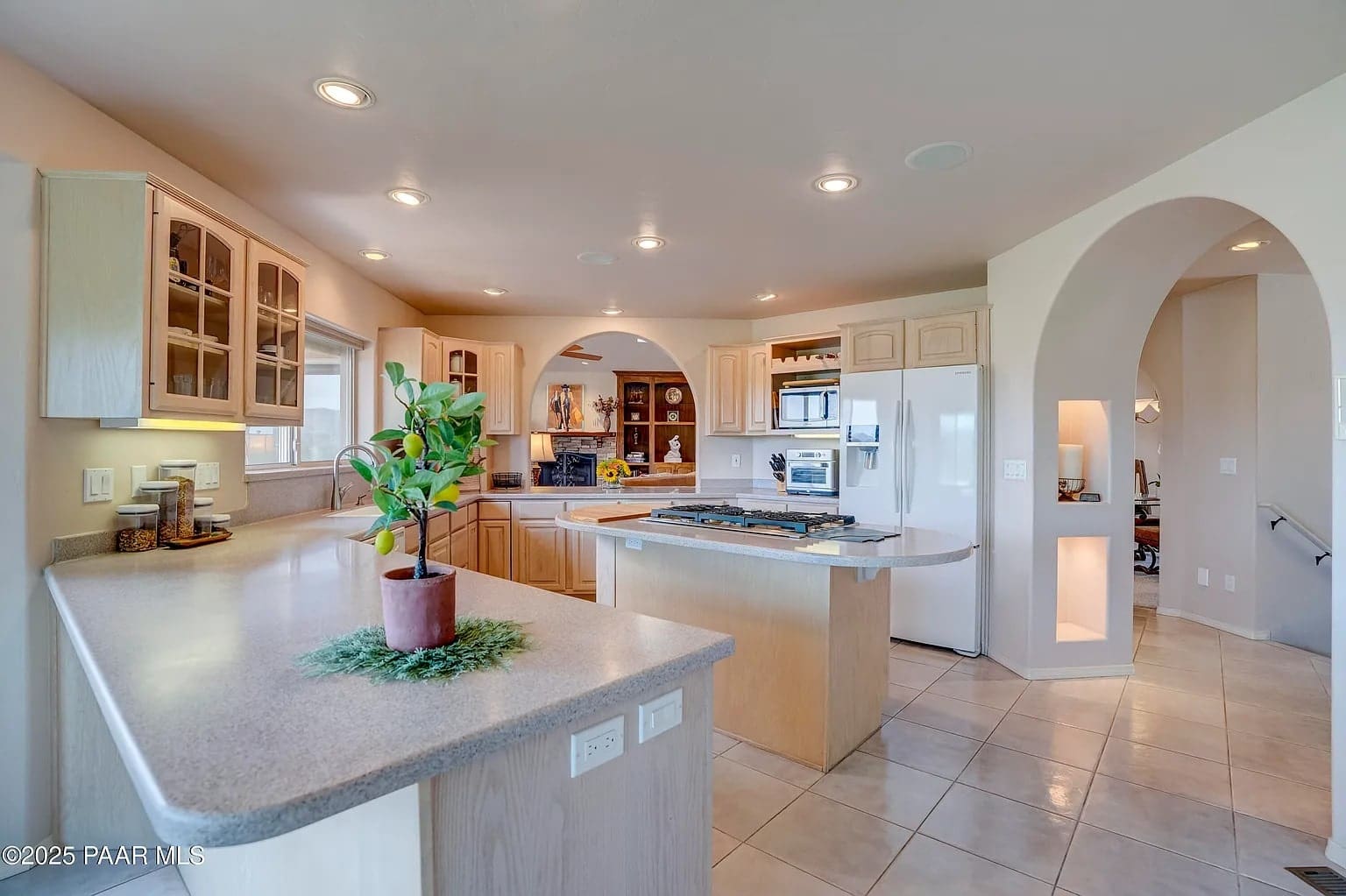 Spacious kitchen with light wood cabinets, island, and modern appliances. Arched doorway leads to another room.
