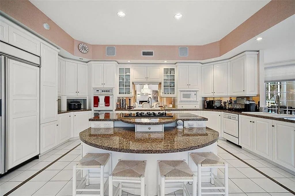 Spacious kitchen with white cabinets, central island, and modern appliances, featuring a pink accent wall.
