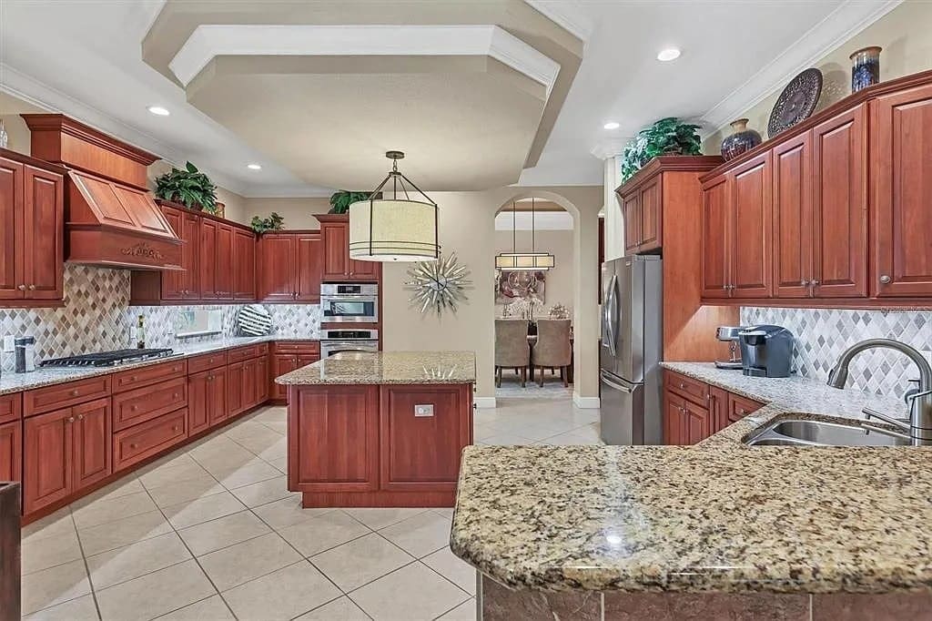 Spacious kitchen with wooden cabinets, granite countertops, island, stainless steel appliances, and decorative plants.
