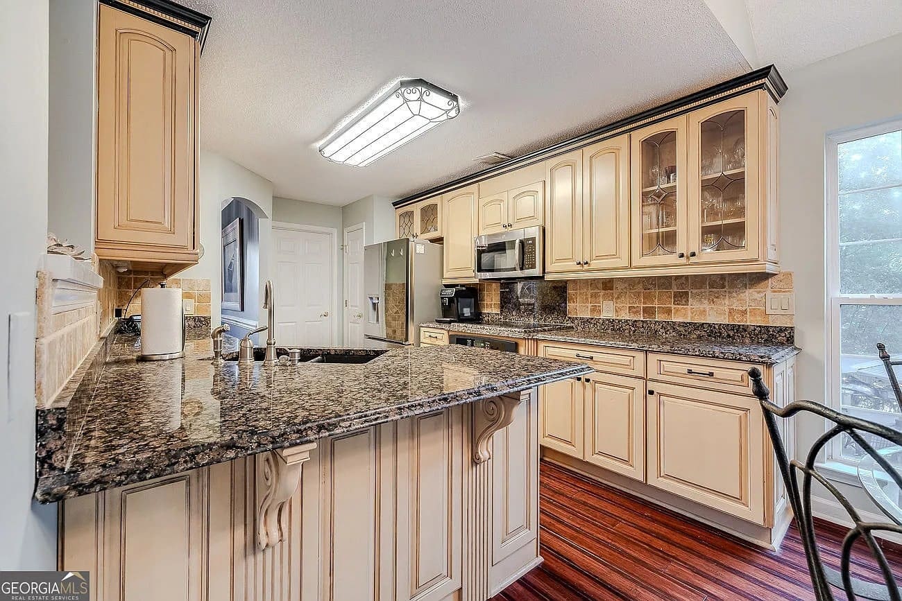 Modern kitchen with granite countertops, wooden cabinets, stainless steel appliances, and hardwood flooring.
