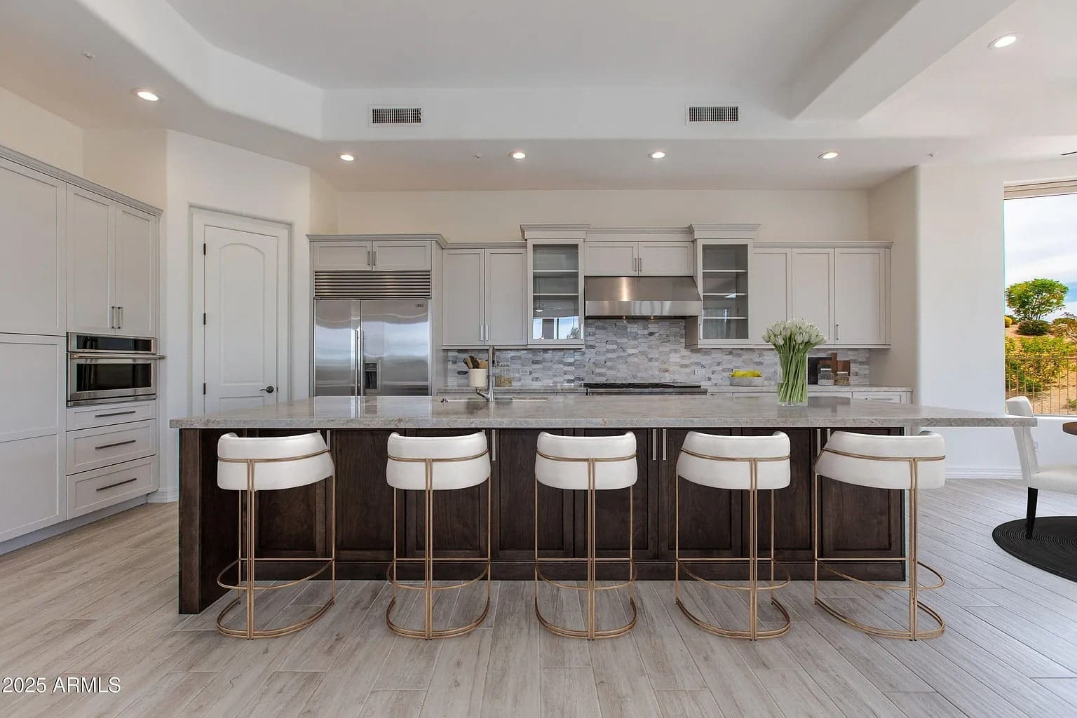Modern kitchen with a large island, bar stools, stainless steel appliances, and light wood flooring.
