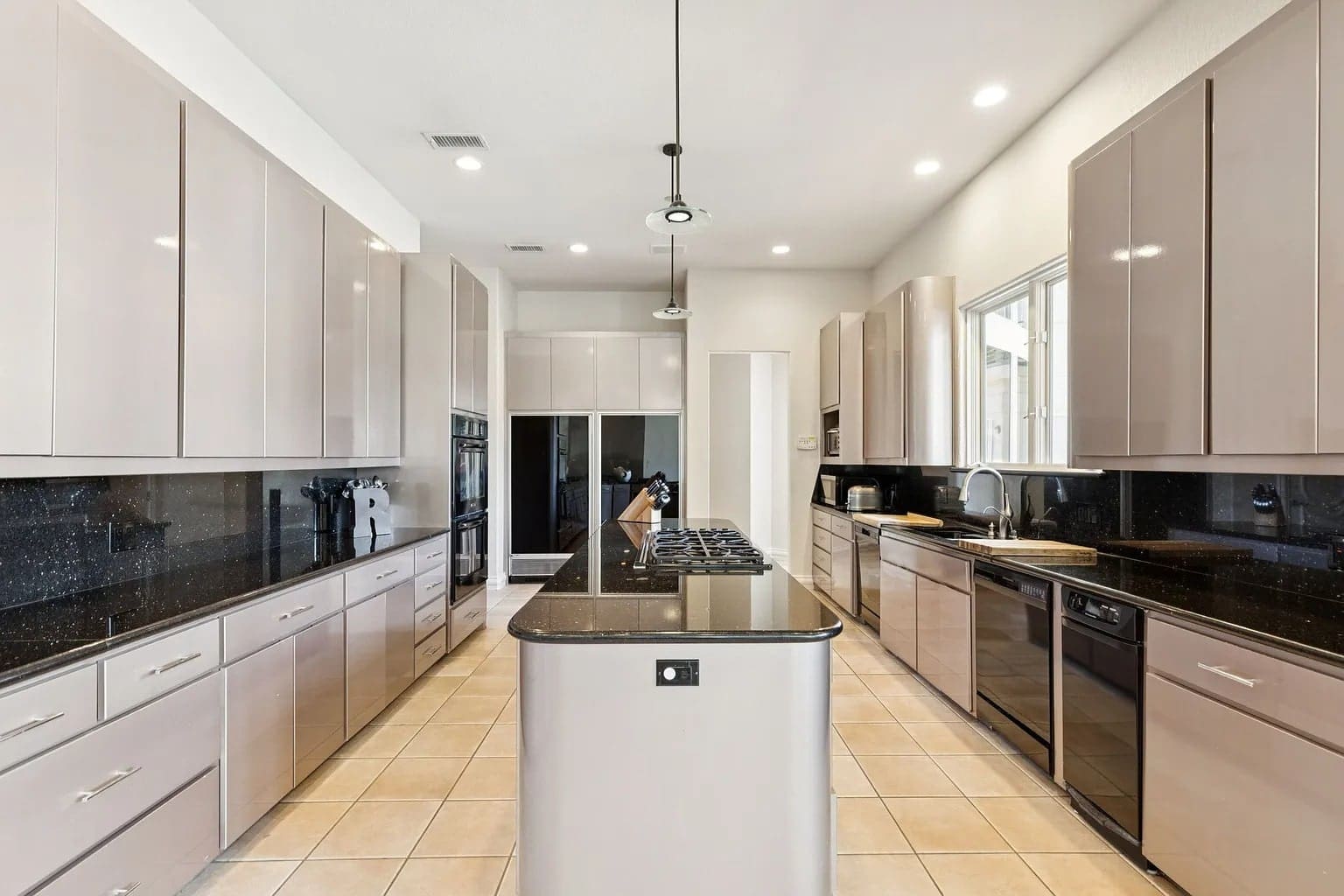 Modern kitchen with beige cabinets, black countertops, island with stove, and stainless steel appliances.
