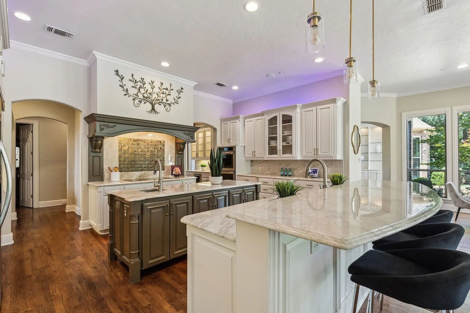 Modern kitchen with marble countertops, dark wood island, white cabinets, and bar seating. Bright, spacious interior.
