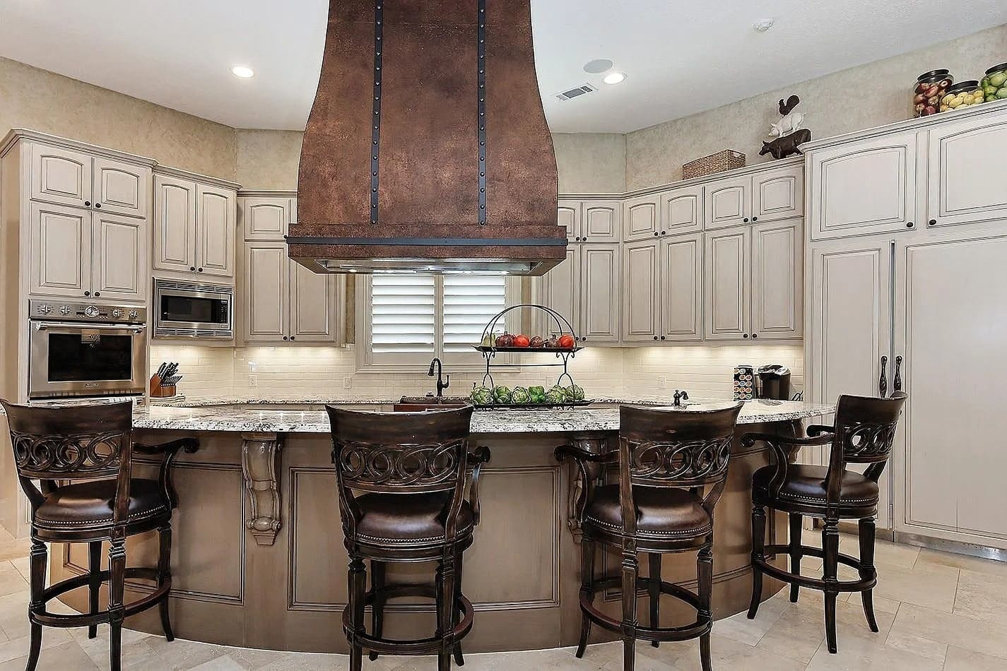 Spacious kitchen with a large island, bar stools, and wooden cabinets.
