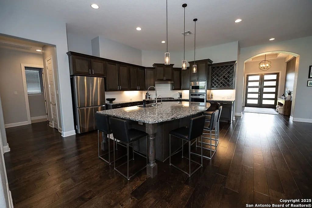 Modern kitchen with dark wood cabinets, large island, stainless steel appliances, and pendant lighting.