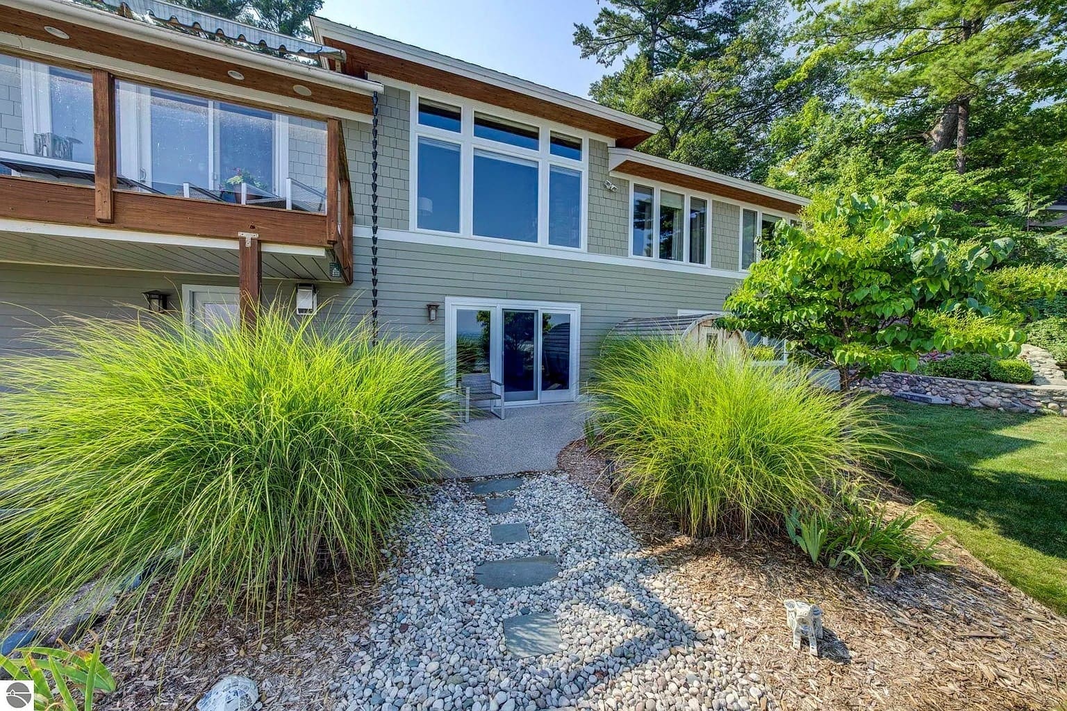 Modern house with large windows, surrounded by greenery and a stone pathway in the garden.
