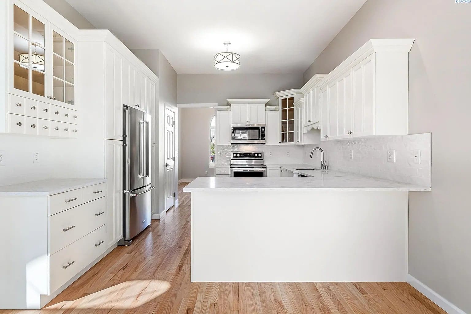 Modern kitchen with white cabinets, stainless steel appliances, and wooden flooring. Bright and spacious.
